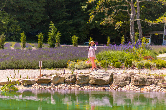 Elegant portrait of young woman standing in purple lavender field near pond in Provence. Fashion and nature combine in a luxurious summer travel concept.