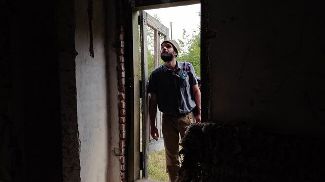Bearded traveler with a backpack entering an abandoned building and looking around