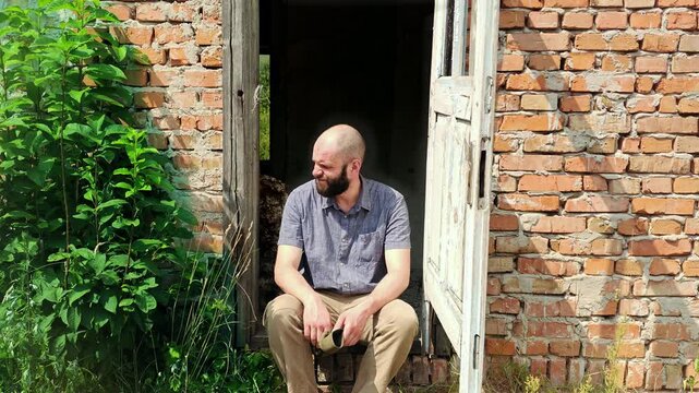 Tired male traveler sitting on the doorstep of an abandoned brick building and resting