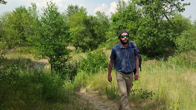 Bearded male hiker with a backpack walking along a nature trail, front and back view