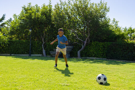 African youth male running across neat garden lawn wearing blue tee chasing black white soccer ball