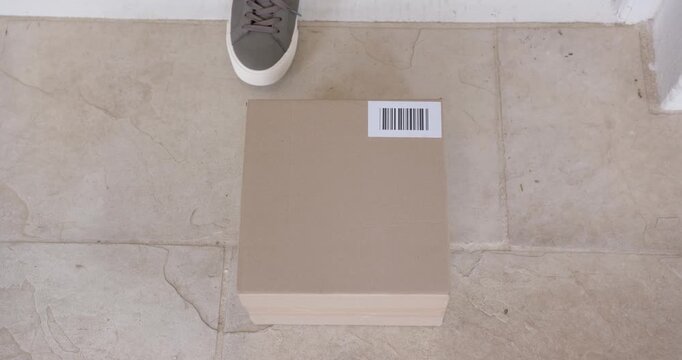 African American man spotting parcel with barcode, stepping on tiled doorstep, reaching and lifting