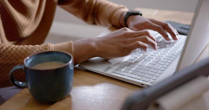 African American man reaching for keyboard, typing on white laptop at table tan sweater mug working