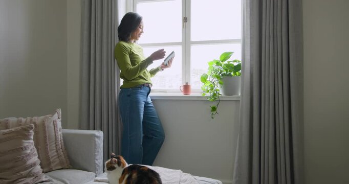 African American woman placing tablet on sill, reaching for pink mug, sipping, gazing out to rest