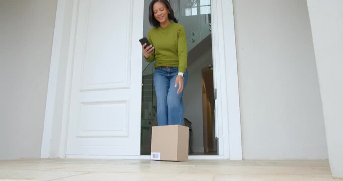 After delivery ping African American woman opening front door checking phone lifting box barcode