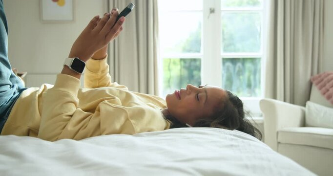African-American woman lying in bed in yellow top using phone, cat settling on lap, lowering phone