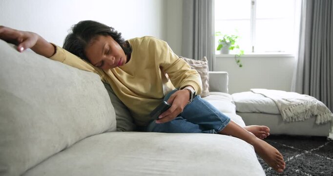 African American woman placing phone on cushion, sitting on sofa at home, looking at window