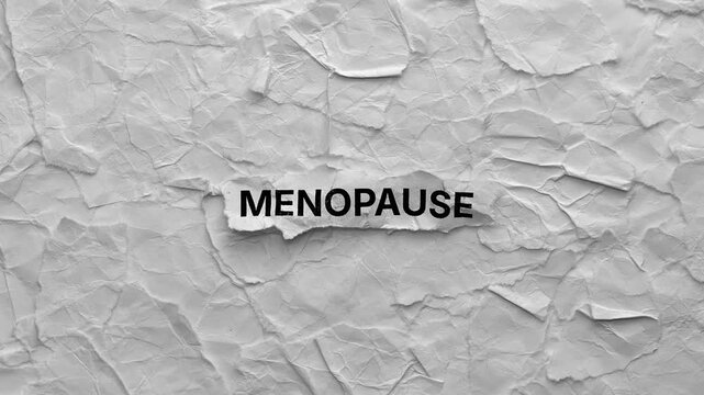 Crumpled piece of paper with word Menopause on torn crumpled white paper pieces background. Zoom in.