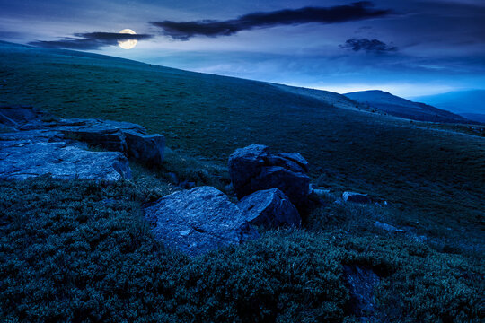 alpine meadow in summer nature at night. full moon over wild grass and grey rocks in carpathian landscape. mountain scenery of perechyn district, ukraine. mysterious fantasy