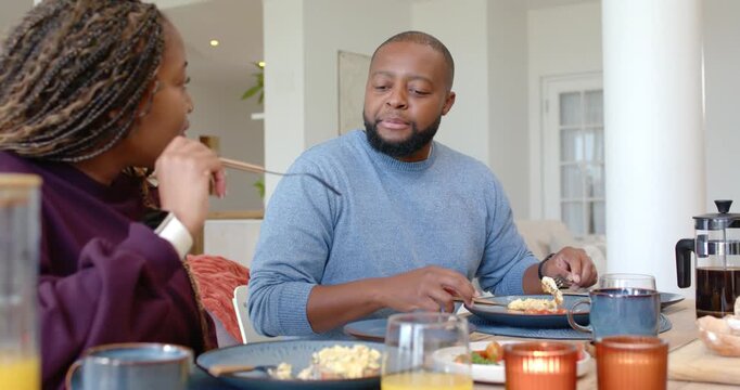 African couple sitting at dining table, man cutting food while woman teasing and feeding with fork