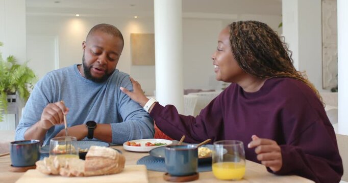 African American couple sharing meal at table, woman touching arm playfully, man feeding tomato