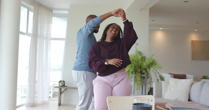 African couple reaching hands leading spin and laughing while stepping near windows being playful