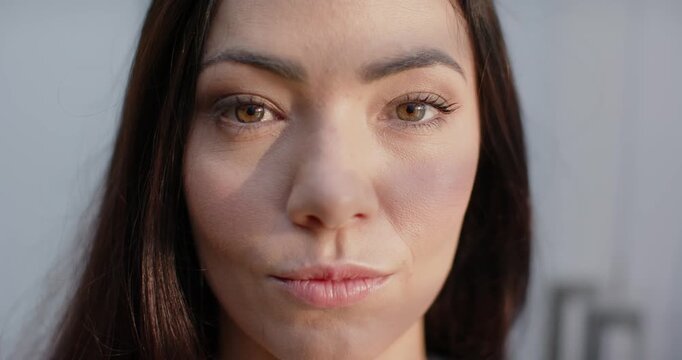 Female facing camera holding direct gaze relaxing face and smiling under diagonal shadow in room