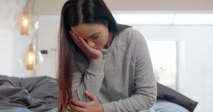 Adult woman sitting on bed in grey sweatshirt plaid pants holding forearm covering mouth breathing