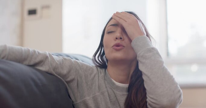 Female sitting on sofa after stress, wearing light grey sweatshirt, lowering hand, reclining