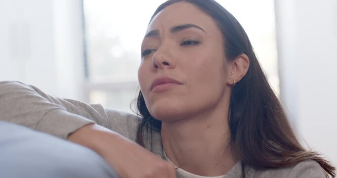 Woman sitting on couch near bright window taking breath, lowering chin, processing grief in sweater