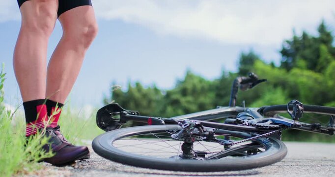 Biker fixes flat tire on road bike during ride in nature on sunny day with clear sky and green trees in background