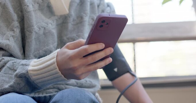 Woman in gray-sweater BP-cuff, holding purple phone on couch after monitor showing result smiling