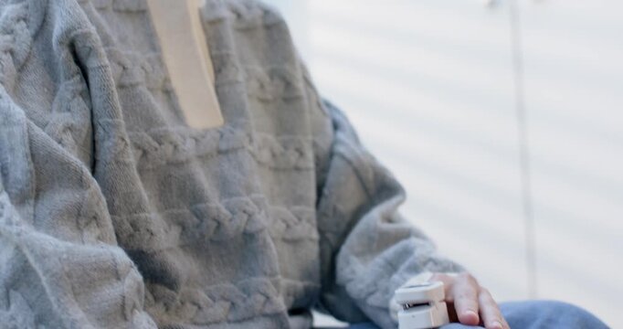 Camera pulling up, sweater-clad Asian woman, stapler on knee, lowering gaze, resting to nap at home