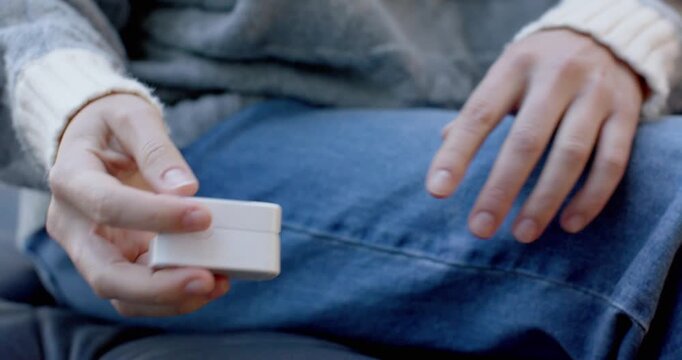 Woman in sweater and jeans tapping pulse oximeter on couch, clipping on finger, checking oxygen