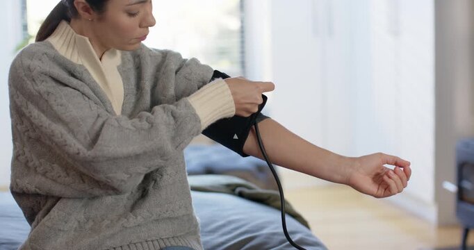 Adult woman preparing for BP check on couch, rolling sleeve, fitting cuff and aligning tubing