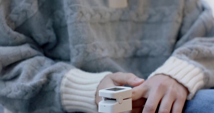 Adult female placing white fingertip clip checking oxygen while sitting at home in grey sweater
