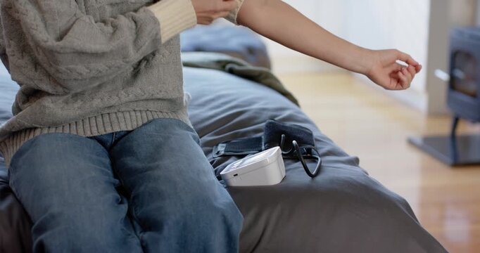 Woman in grey sweater rolling sleeve reaching for black cuff to monitor at home monitoring BP