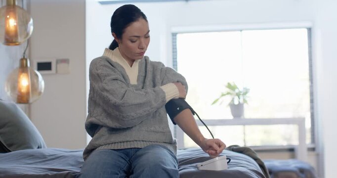 African-American woman reaching for monitor on bed in gray sweater, preparing cuff to check BP