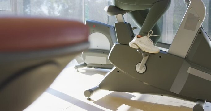 African American woman starting workout, pedaling on exercise bike at gym wearing green leggings