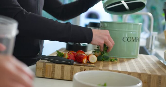 Female friends preparing fruit in kitchen, main woman gathering trimmings into green composter