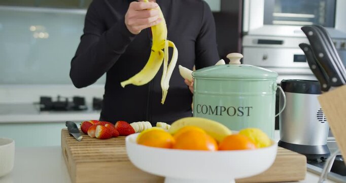 Making fruit, woman in black top peeling banana, lifting lid, dropping peel into compost in kitchen