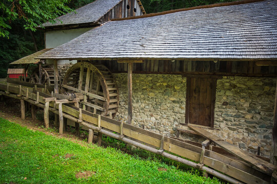 Rustic old watermill with wooden wheel and stone walls in a lush green forest setting.