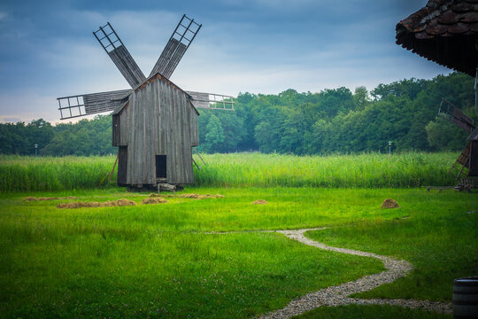 Rustic wooden windmill set in a lush green field under a cloudy sky.