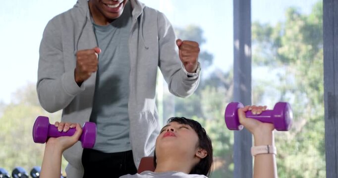Male trainer placing hands at wrists, spotting client pressing purple dumbbells on bench for form