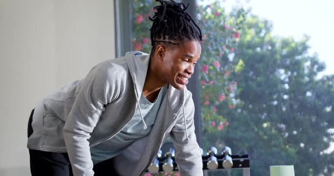 African American man leaning and gripping metal dumbbell doing one-arm rows in home gym for fitness