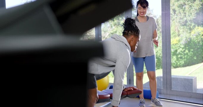Trainer and client in home gym gesturing to start, bracing on bench rowing dumbbell for strength