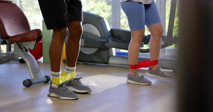 African American couple doing side band walks with ankle loops pulling outward in gym toning hips