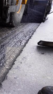 Asphalt Resurfacing Process and Roadworkers Tools Low Perspective. Ground-level shot showing three rows of asphalt paving machine wheels during hot tarmac laying. Road reconstruction.