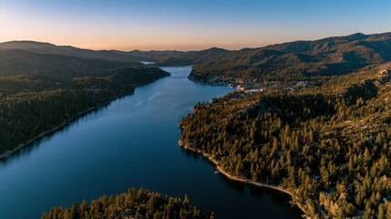 Obraz premium Golden hour drone panorama over a scenic alpine lake with forested shores and a distant lakeside community