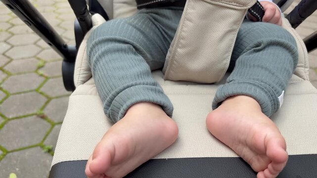 A child under one year old in a stroller. The bare feet and lower legs of a baby sitting in a beige stroller.