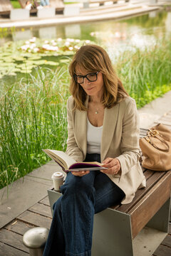 Mature blond haired woman reading a book in a peaceful city park