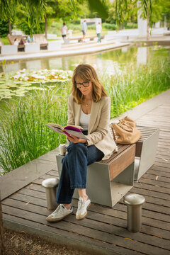 Mature blond haired woman reading a book in a modern city park