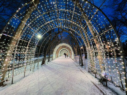 Couple Walking Through Illuminated Light Tunnel of Christmas Lights in Snowy Winter Park at Night