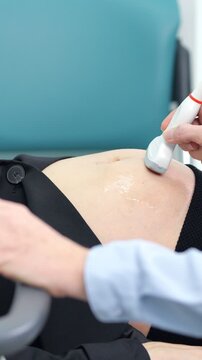 Medical professional moving an ultrasound transducer over a patient's abdomen covered in gel during a diagnostic examination in a modern clinic, checking the health of internal organs