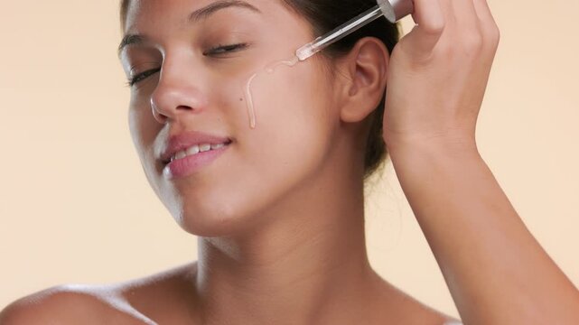 Beauty portrait of skincare model applying face serum on her cheek on beige background | Anti acne skincare video concept