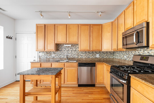 A kitchen with wood cabinets, tiled backsplash, small island, and black and stainless steel appliances.