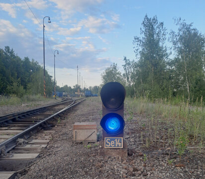 Blue railway signal beside railroad tracks under evening sky.