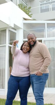 Vertical video: African American couple holding new keys, celebrating new home outside house