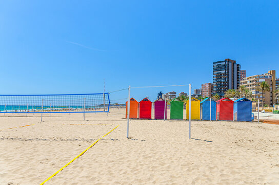 Playa de San Juan beach in Alicante city, wooden colorful storage huts for sports equipment and sports courts with volleyball net on sandy beach of Mediterranean Sea coast in sunny summer day, Spain