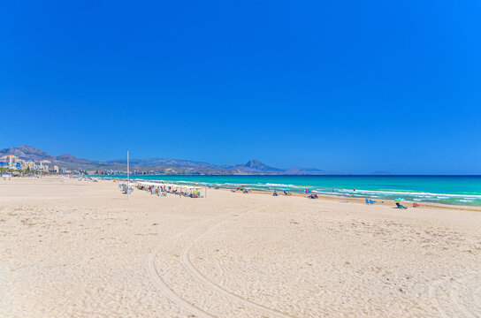 Playa de San Juan beach in Alicante city Campello town, people relaxing on sandy beach of Mediterranean Sea coast Costa Blanca coastline in sunny summer day, and mountain range background, Spain